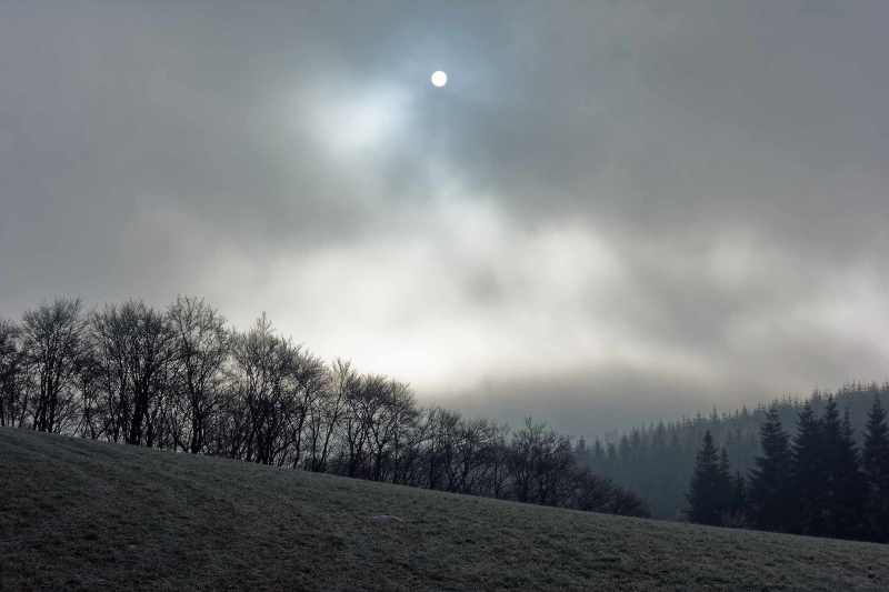 Die Sonne scheint durch dichte Wolken auf eine winterliche Berglandschaft, Deifeld, Hochsauerland